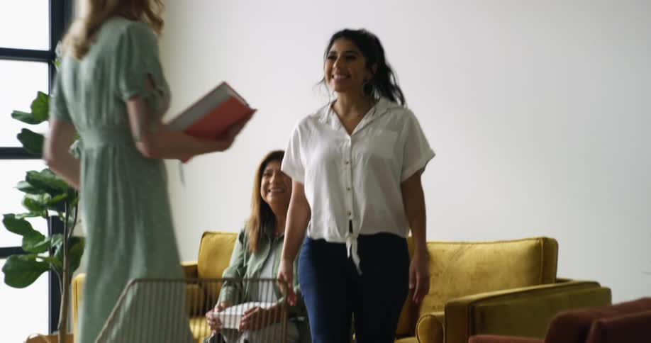 Two women sitting on a couch greeting another woman