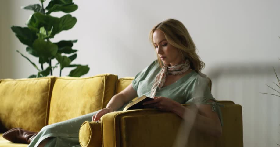 A woman with a scarf sitting on a couch reading a book