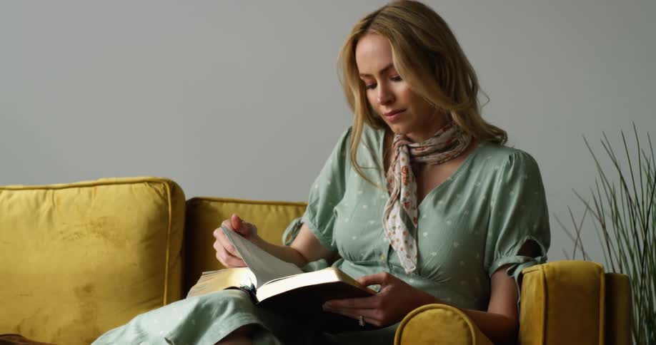 A woman is reading a book on the couch