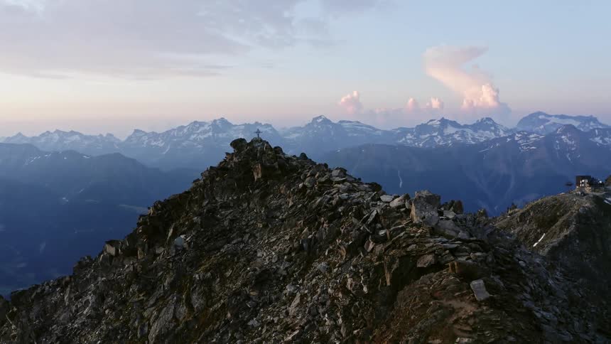 A small cross sits on the peak of a rocky mountain