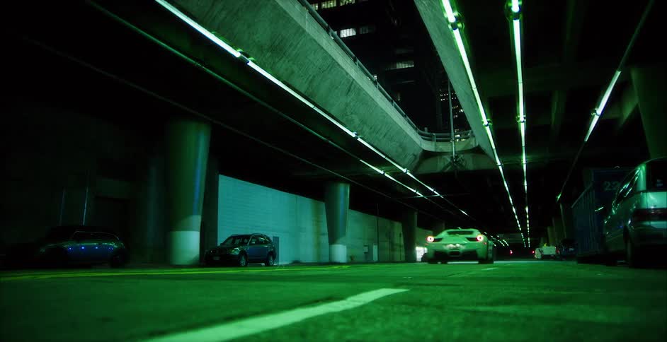 A car travels quickly along a road under an overpass in a city at night