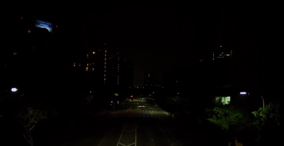 A white car drives down a city street at night