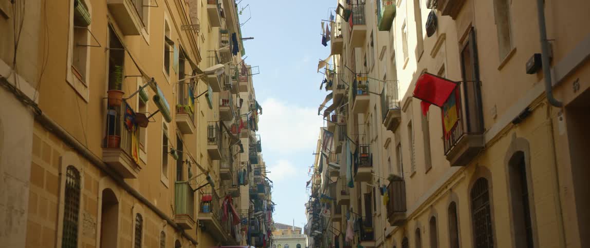 Person walks inside from balcony in one of buildings that face each other closely along the block under a cloudy sky