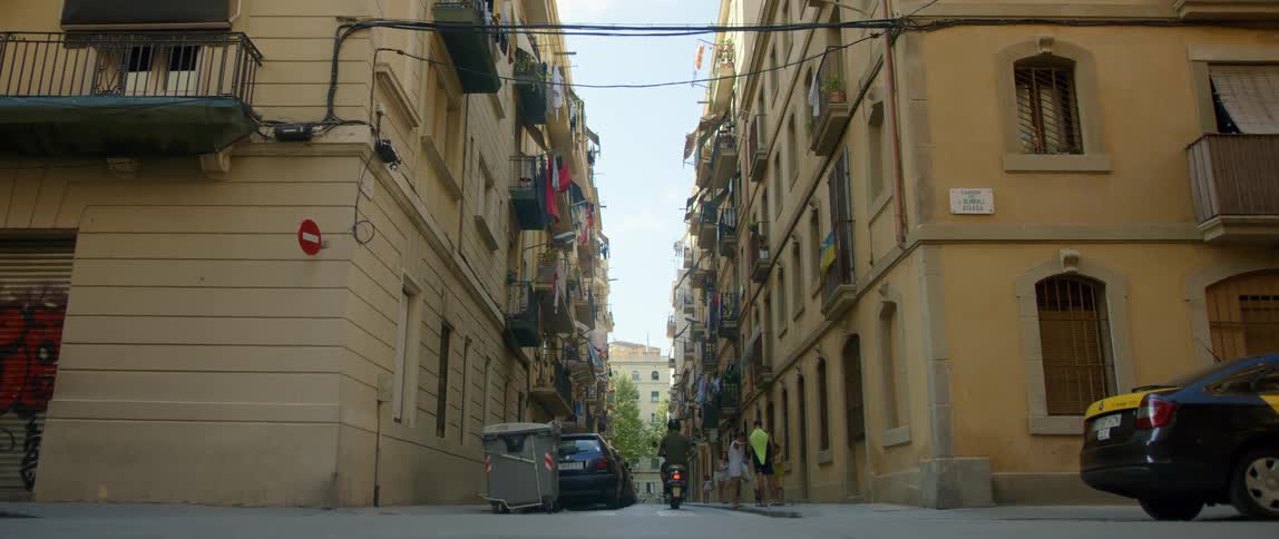 A man rides his scooter down an alley between two apartment buildings