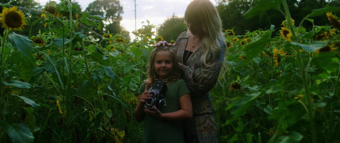 A child is holding a camera as a woman brushes her hair