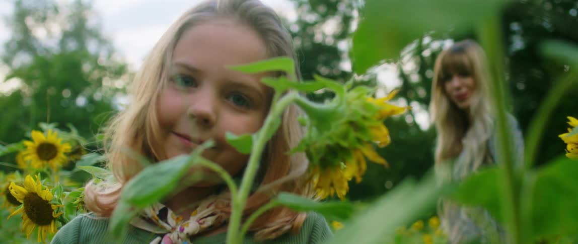 A mother and daughter are standing in the sunflower patch