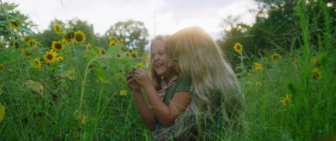 A mother hugs her daughter in a field of sunflowers and they laugh