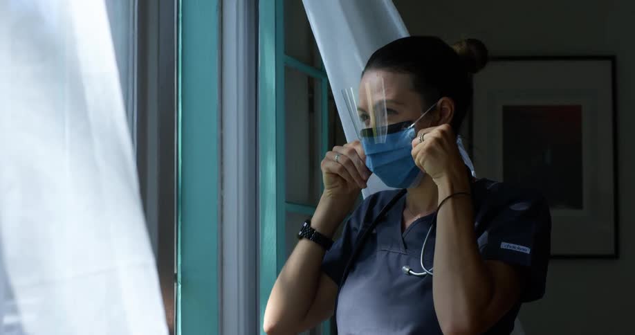 A woman with a mask a face shield a stethoscope and scrubs