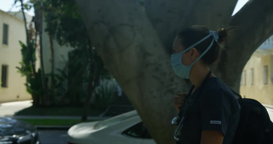 A nurse walks through her neighborhood in scrubs and a face mask