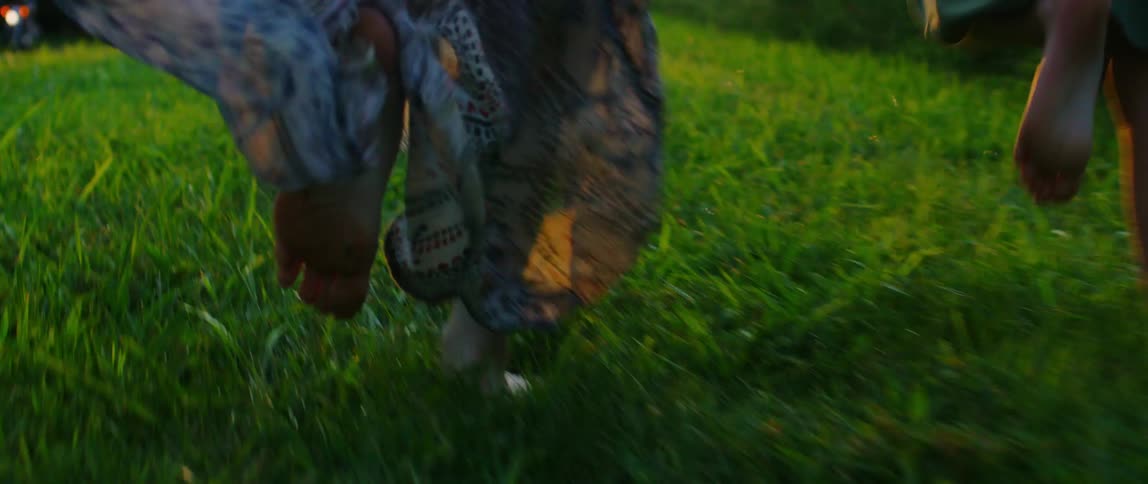 A mother and her daughter run barefoot in the grass while holding hands