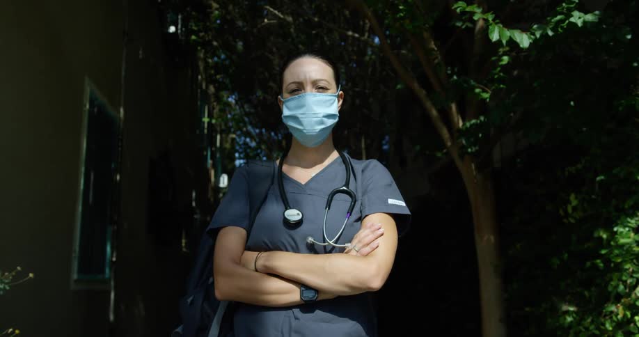 A nurse is standing in the shade by a home
