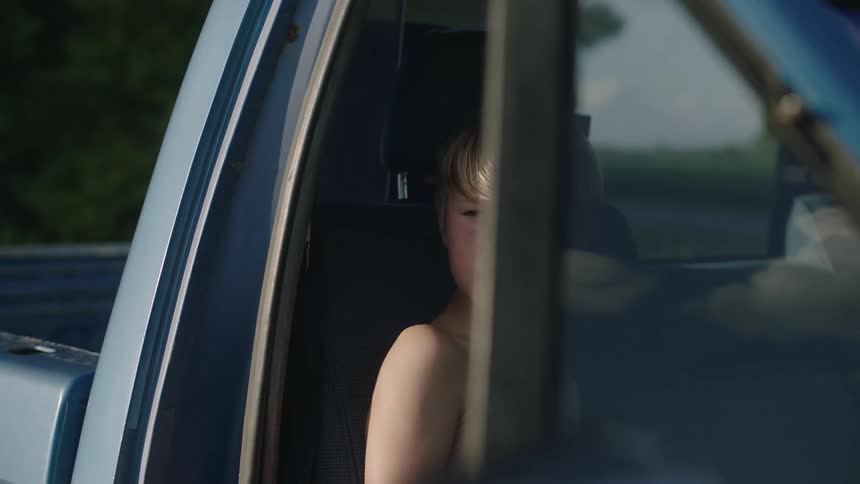 A man grabbing a backpack aggressively from a truck with a boy sitting down