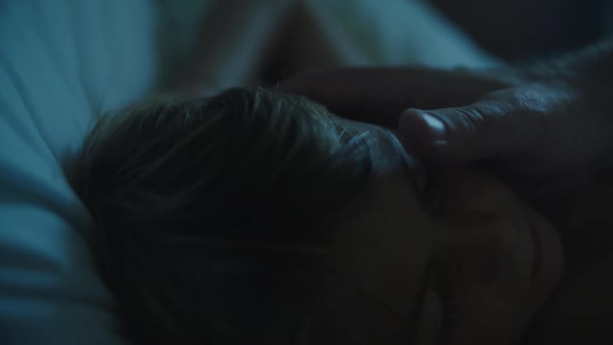 A young boy sleeps in bed as his father gently caresses the boys hair and cheek