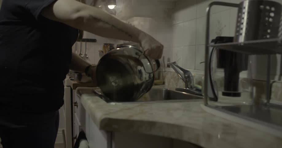 A woman empties a boiling pot of food into a strainer in the sink