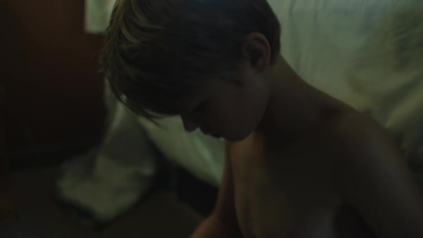 A boy sitting on the floor of a bedroom removes a bundle of cash and a crumbled piece of paper from his backpack