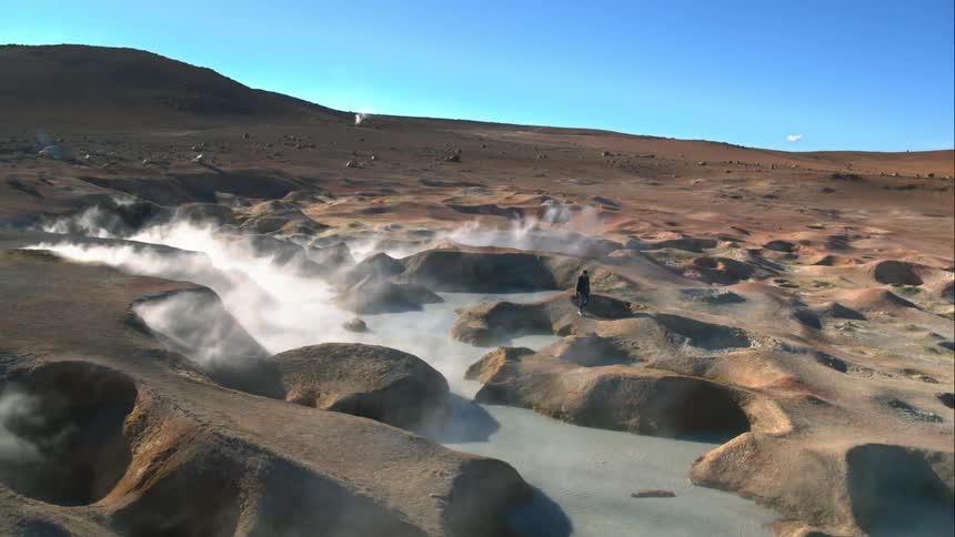 A man walks across steaming geysers and takes photos