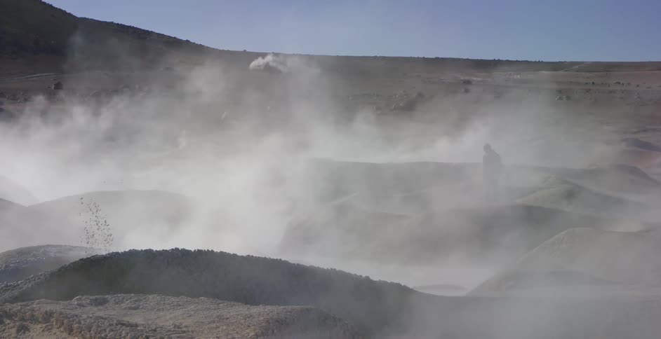 A man carrying a camera walks past geysers