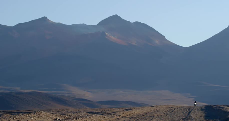 A person riding their motorcycle at the base of a mountain