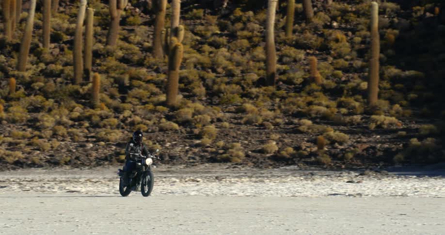A person drives their motorcycle over the sand