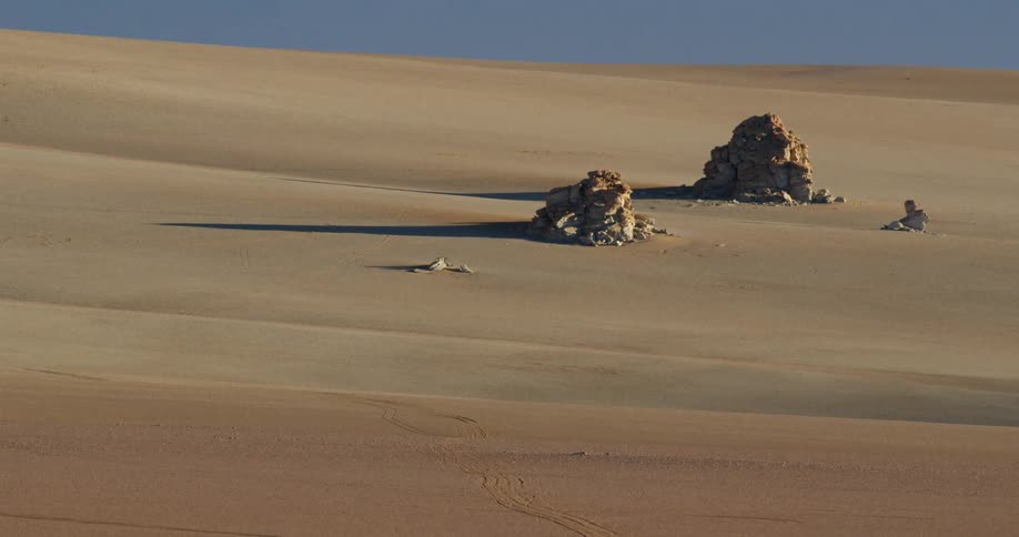 Piles of rocks are casting shadows on a desert hill during the day