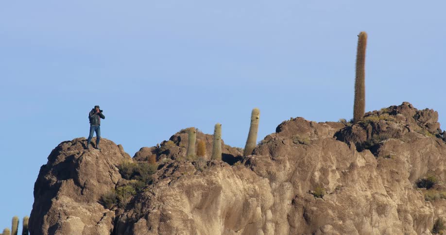 A photographer takes a photo while standing atop a rock formation in the desert on a sunny day