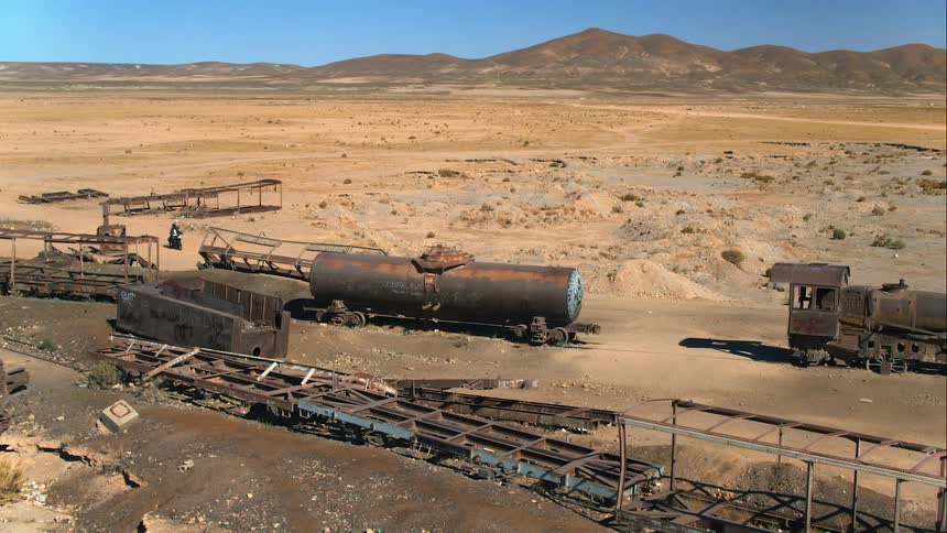 Aerial of motorcycle driving through pipeline of abandoned trains