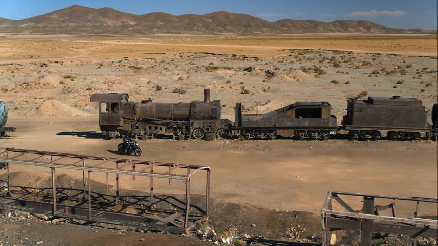 A person on a motorcycle rides beside an old abandoned train