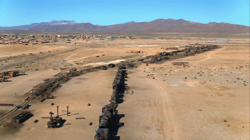 Aerial view of a train wreck with a town and mountains in the background in the desert