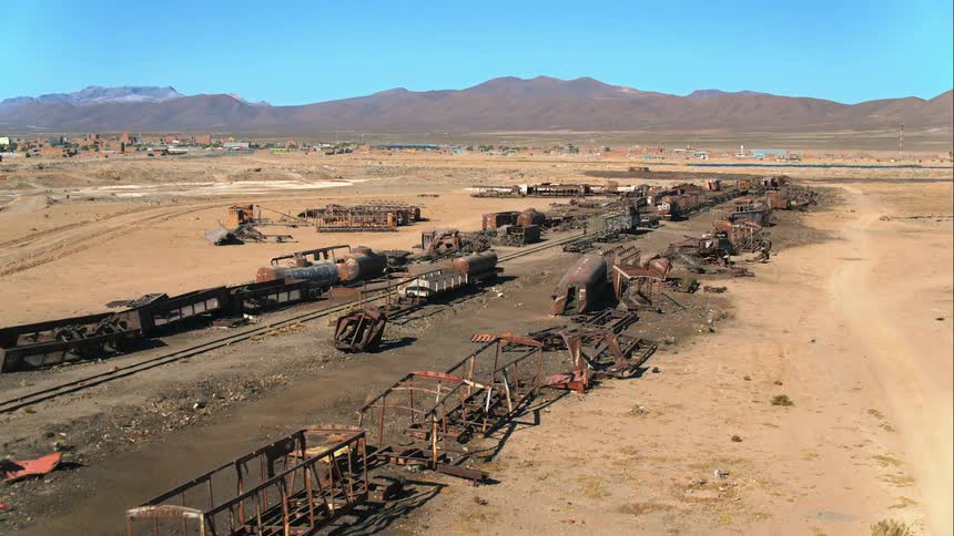 A train rail surrounded by wreckage running through the desert on a sunny day