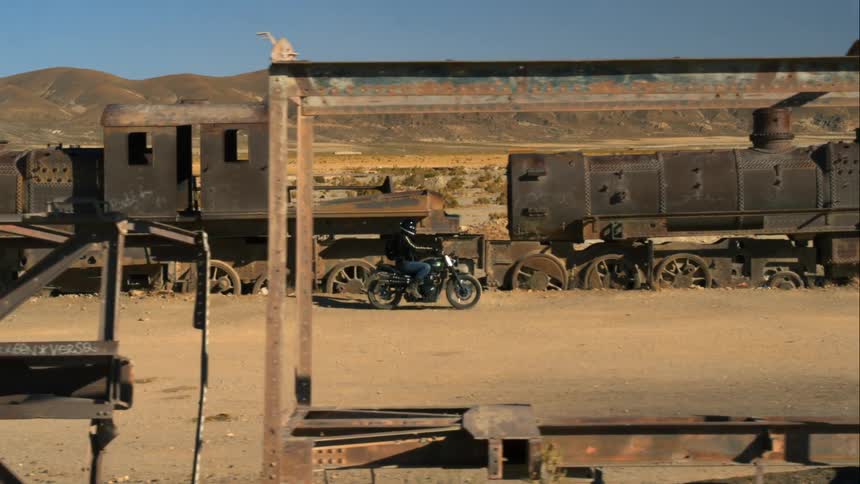 A person with a backpack and a helmet riding a motorcycle next to an abandoned train