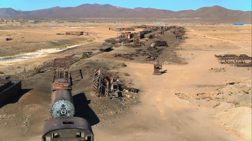 Oldabandoned train sits on train track in desert with town and mountains in distance