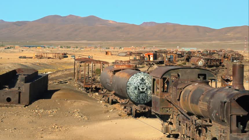 Aerial view of a train wreck with a town and mountains in the background in the desert