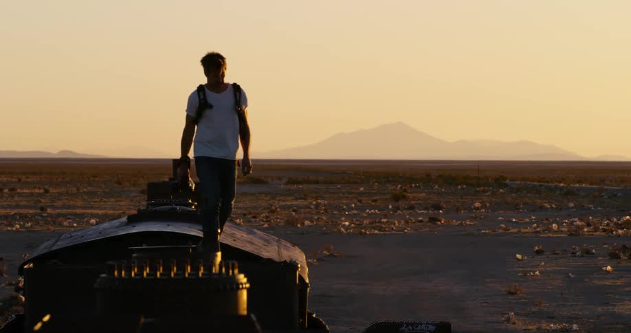A photographer walks around a derelict train in the desert in the evening a prepares to take a photo