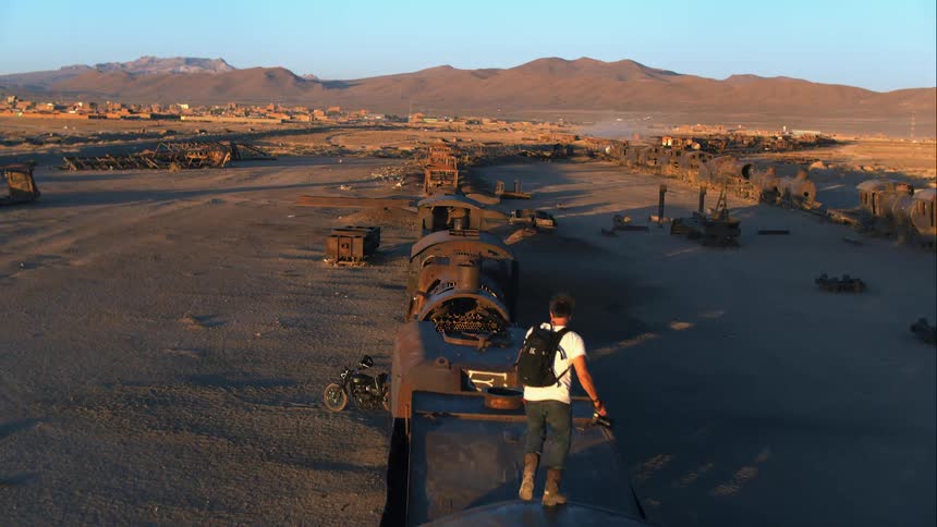 A man walking across rusted out train parts in the desert