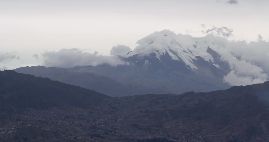 A forested valley sits near a snow covered mountain range
