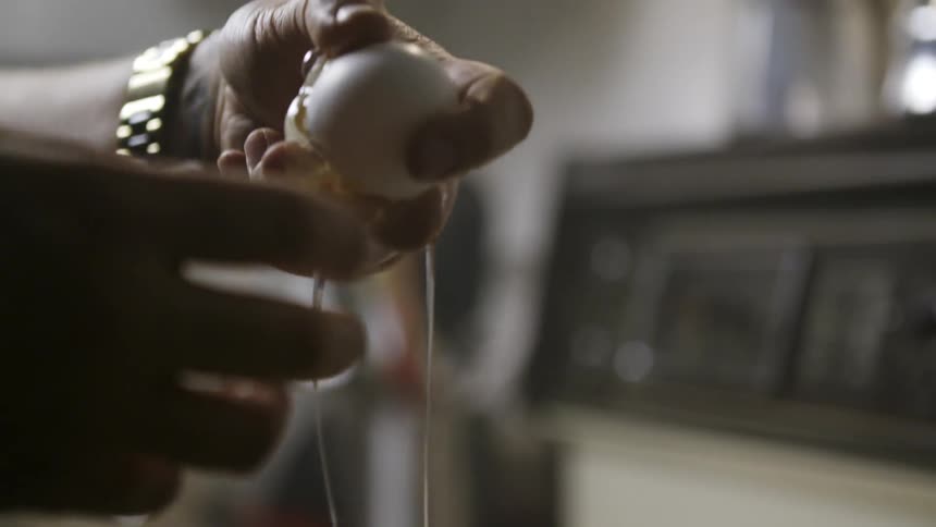 A person cracks an egg and pours it into a silver bowl