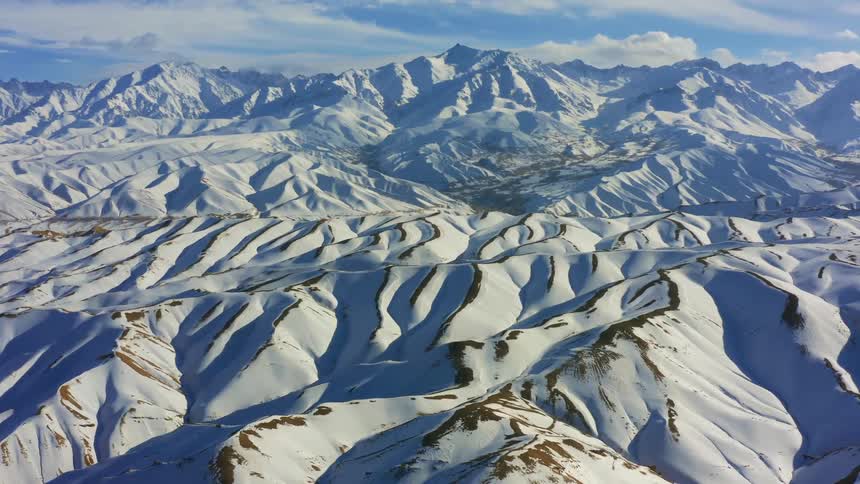 Snow covered ridges and slopes stretch to horizon under cloudy sky
