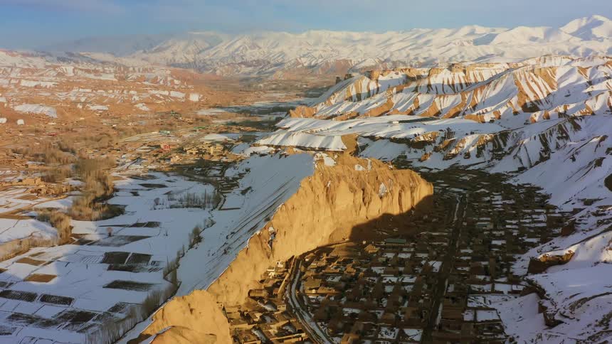 A town near a cliff with snow with a mountain range and the sky in the background