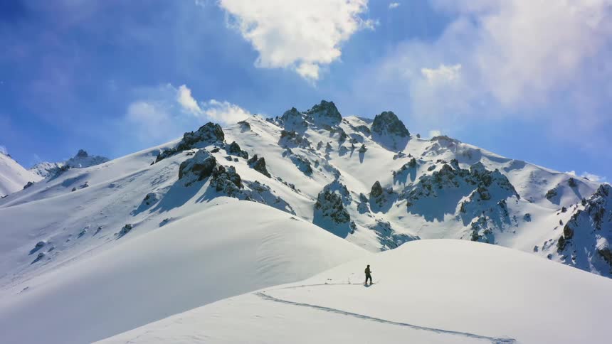 A hiker uses trekking poles to hike across the snow covered top of a mountain ridge