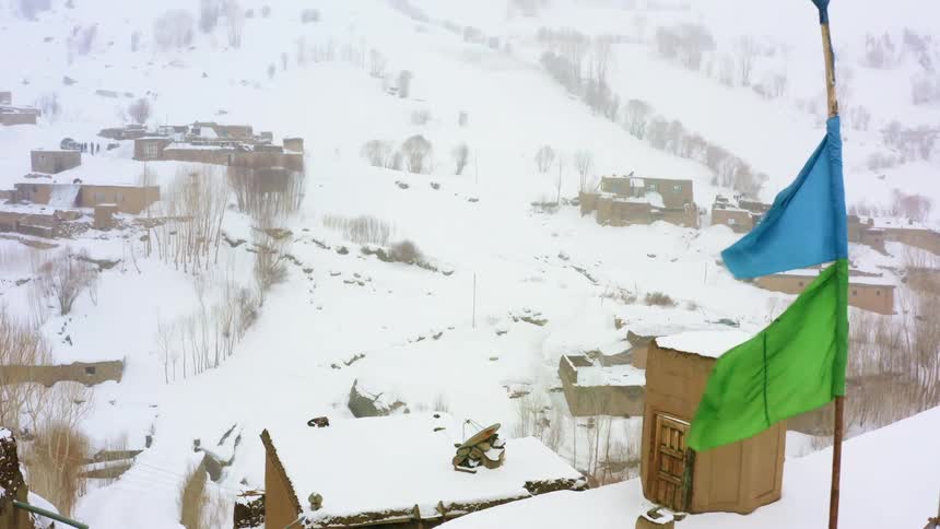 Banners flap on pole in town of snow covered buildings occupying bottom of mountain slope