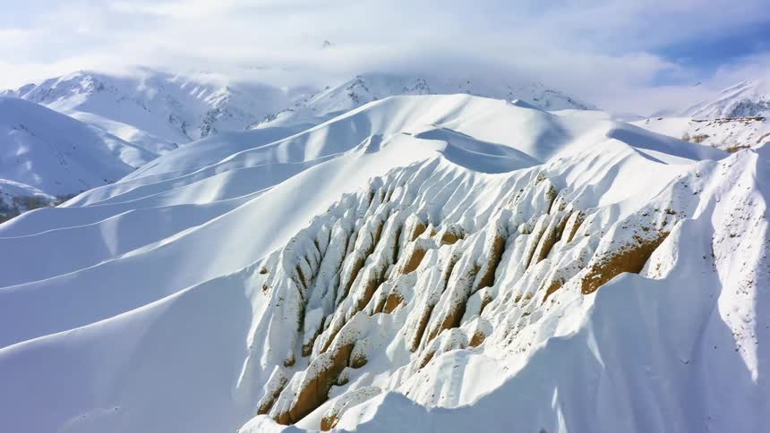 A mountain range covered in snow with the sky and clouds in the background