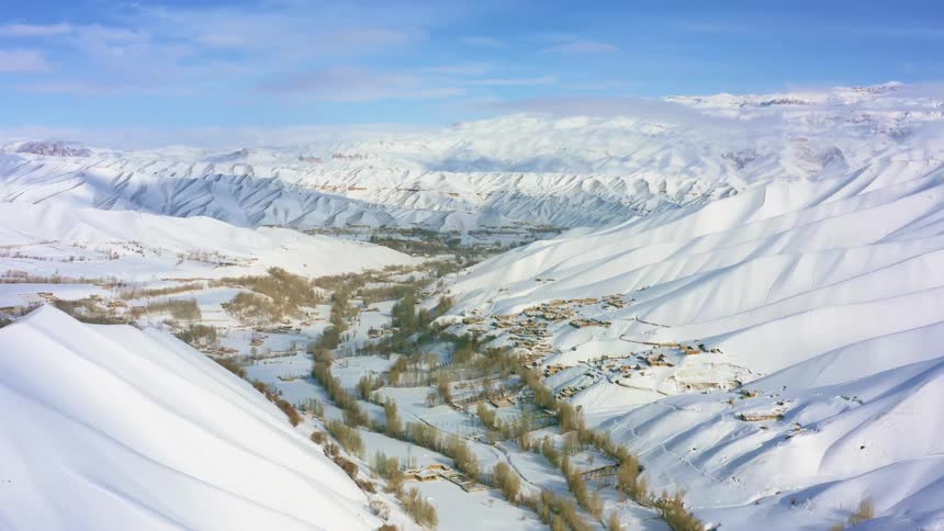 A mountain range covered in snow with the sky and clouds in the background