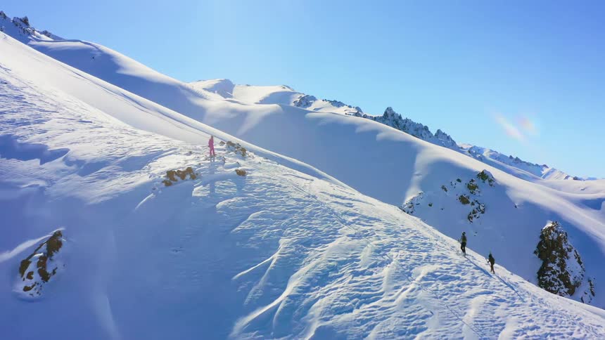 Aerial view of a small group of people climbing the snow covered slope of a mountain range