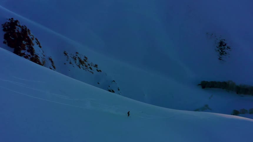 A person skiing down a snowy slope with the sky and clouds in the background