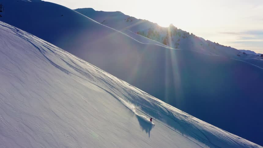 A person skiing down a snowy slope with the sky and clouds in the background