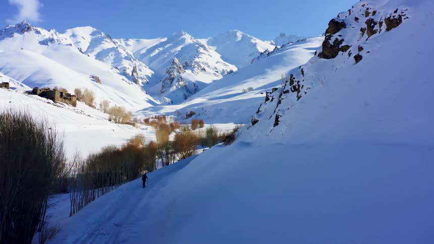 An aerial view of a person hiking in snowy mountains on a winter day