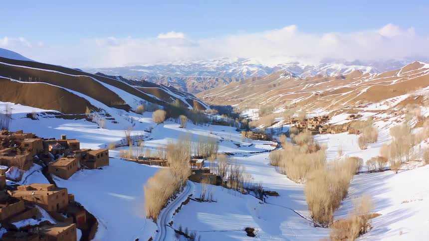 An aerial view of a snow covered valley with rolling hills and a mountain range in the distance