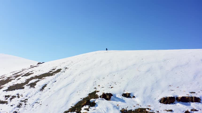 A person standing at the top of a hill waves their arms in the air
