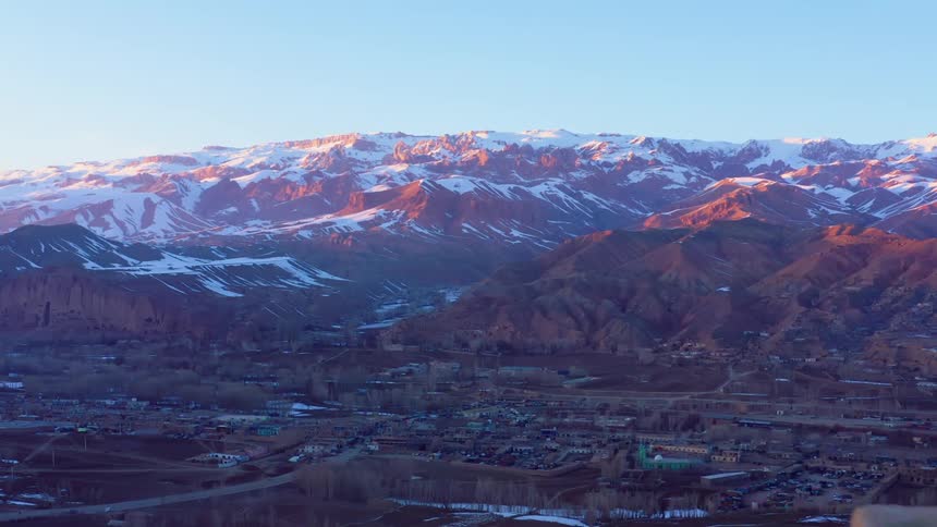 A city in a valley between snow capped mountains on a sunny day