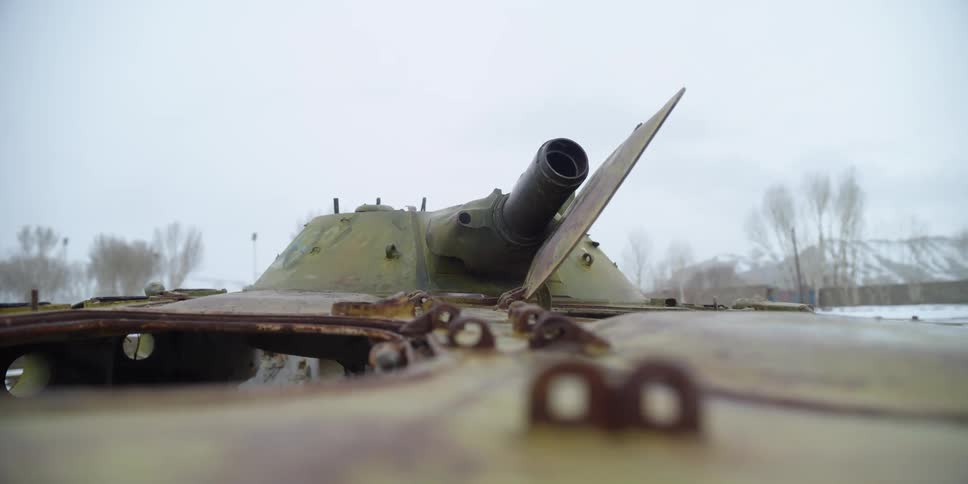 Rusted tank with open hatch sits outside with snow covered mountains on horizon